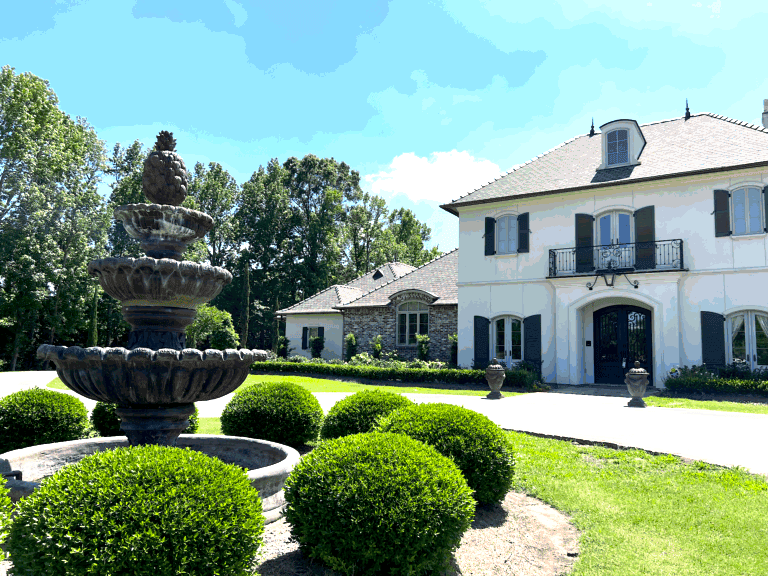A large stone fountain showcases professional Water Feature Installation in front of a two-story house with arched windows and a circular driveway.