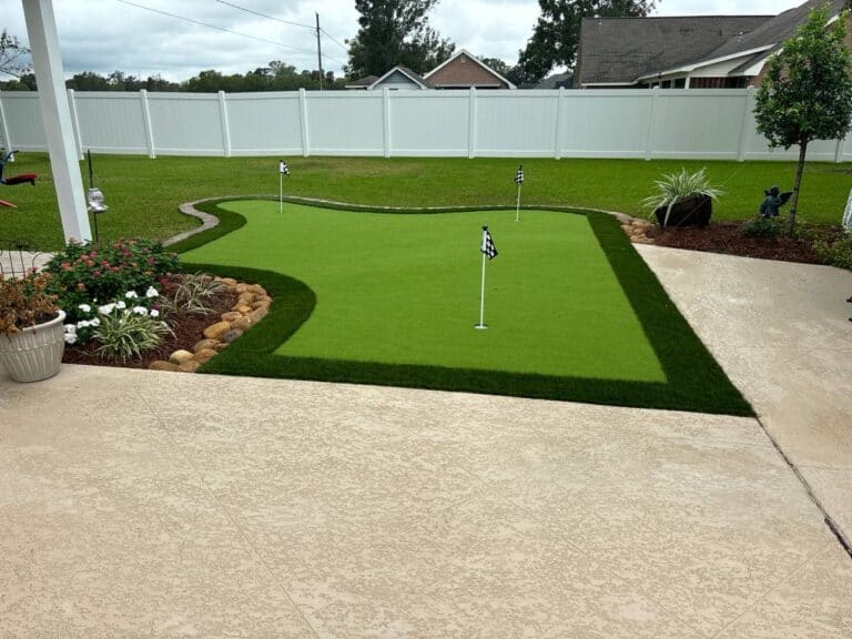 A backyard with Putting Greens, three flags, beautiful landscaping, and a white fence surrounding the yard.