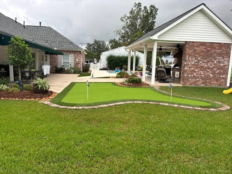 A backyard with putting greens, a patio area, covered outdoor seating, and landscaped plants on a cloudy day.