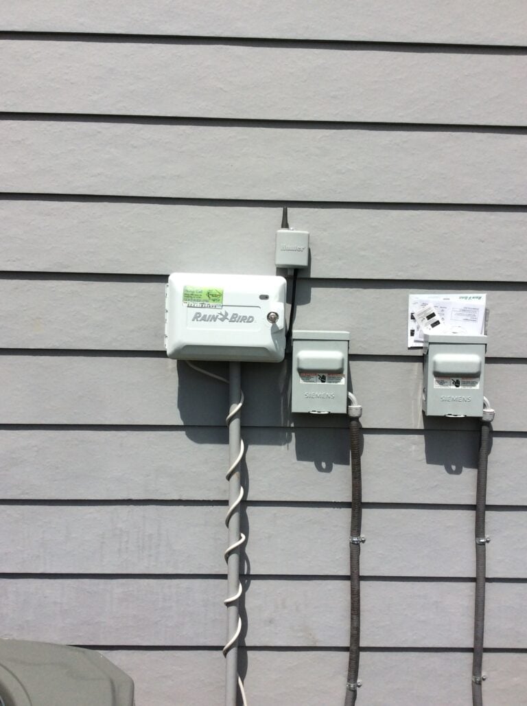 An outdoor wall-mounted irrigation control box labeled 