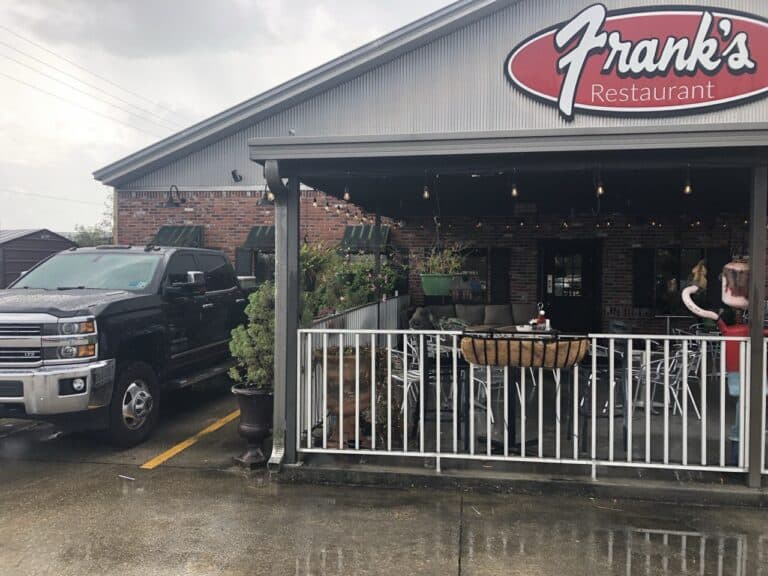 A black pickup truck parked outside Frank's Restaurant, with a covered patio, tables, and chairs visible on a rainy day.