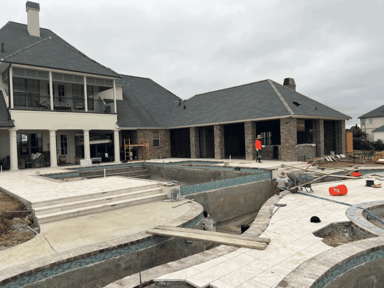 A large house at Lazy Waters with an unfinished backyard pool under construction, workers present, and building materials scattered around.