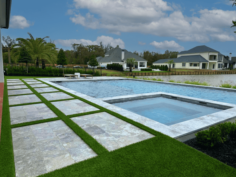 A large backyard with a tiled patio, a rectangular swimming pool, a hot tub, and modern houses in the background under a partly cloudy sky.