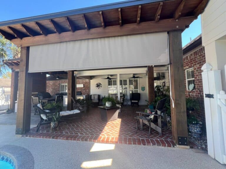 Covered patio with brick flooring, Paradise Palms outdoor furniture, plants, ceiling fans, and a partially closed roller shade by a pool.