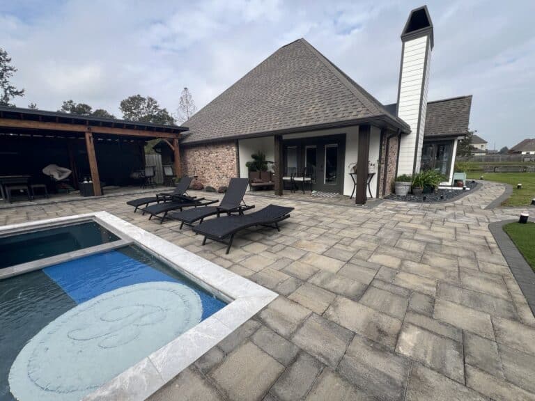 A backyard at Pavillion Pointe with a small pool, black lounge chairs on a stone patio, and a house with large windows and covered seating area.
