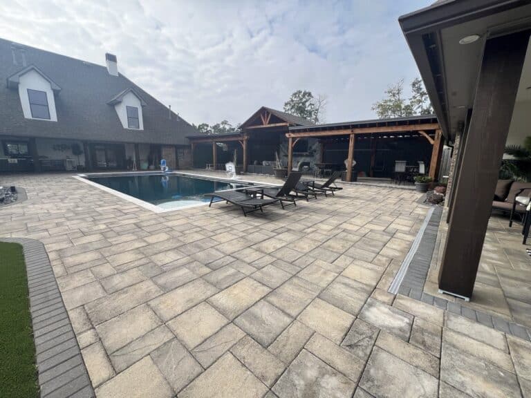 A backyard patio at Pavillion Pointe features a pool, lounge chairs, covered seating areas, and light brown tile flooring on a cloudy day.