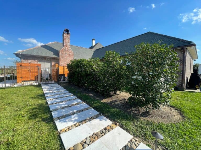 A modern house with a brick chimney, stone walkway, and green shrubs sits serenely under the clear blue sky at Lazy Waters.