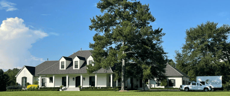 A large white house with dark roof sits behind a tall pine tree; a white truck and trailer add to this unique portfolio piece.