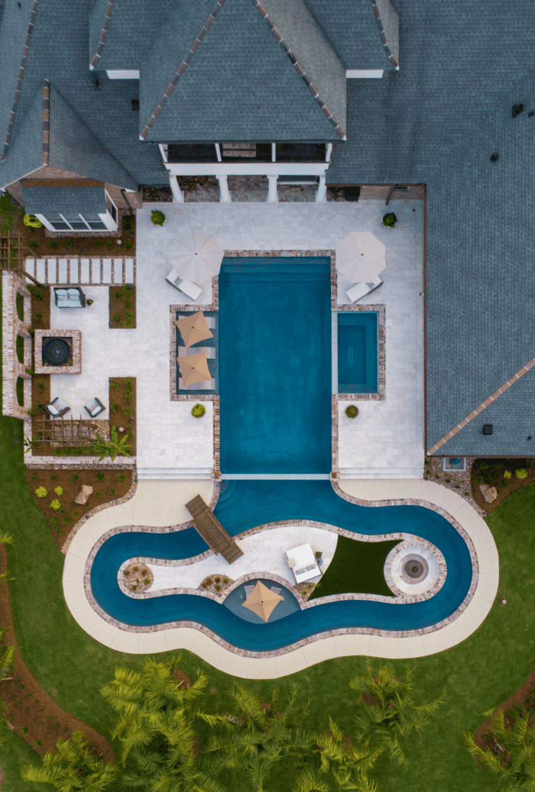 Aerial view of Lazy Waters backyard with a rectangular pool, winding lazy river, lounge chairs, umbrellas, and landscaped greenery.