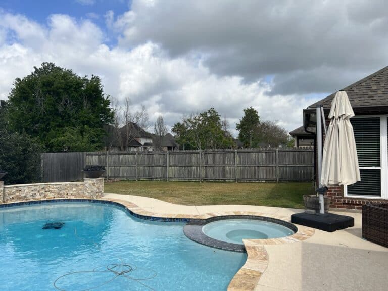 A backyard with a swimming pool, hot tub, patio furniture, and a wooden fence under a partly cloudy sky.